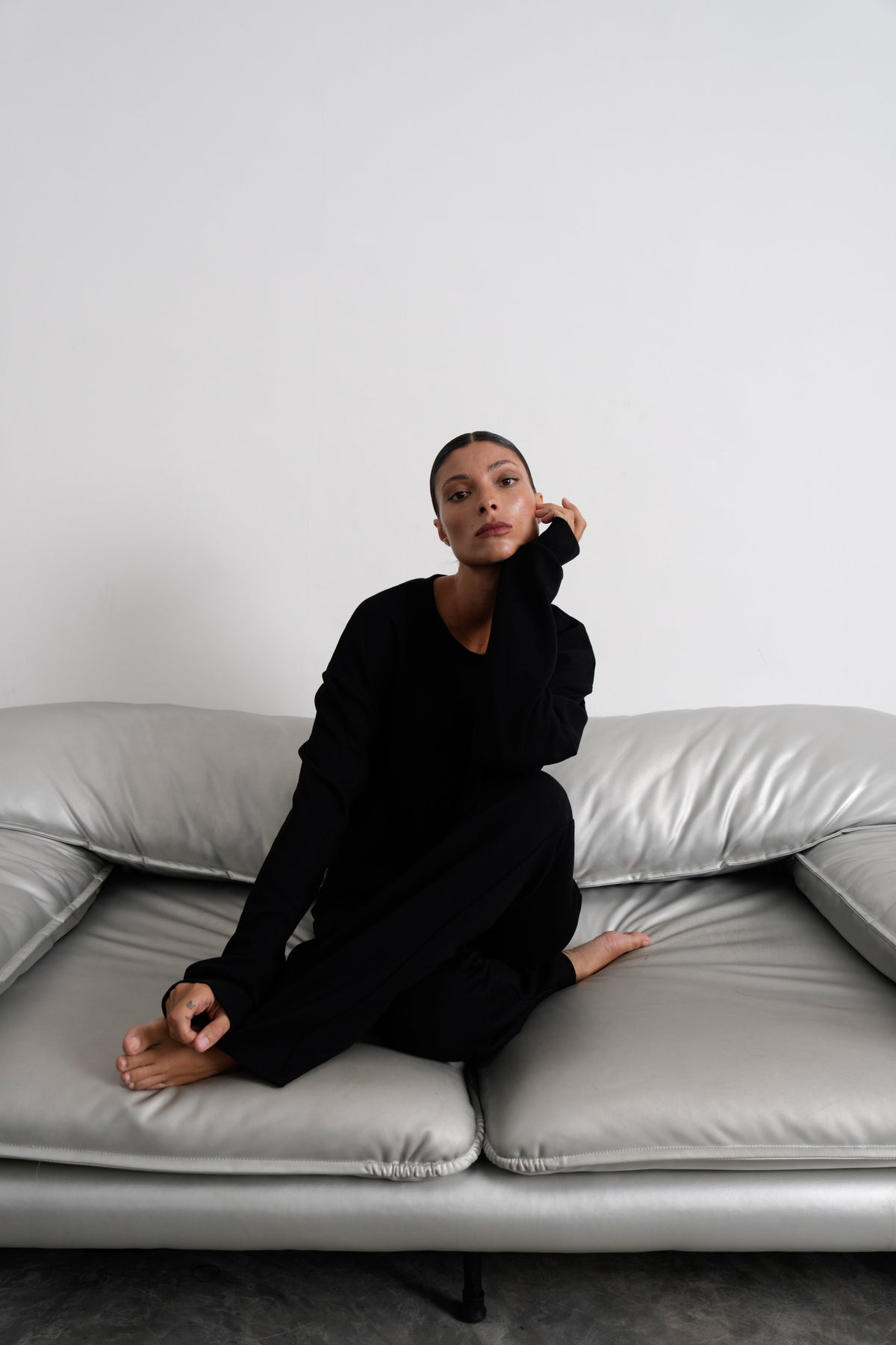 Große Frau im schwarzen Tall Loungewear-Set, barfuß auf einem grauen Ledersofa sitzend